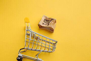 Damaged paper box and shopping cart on a yellow background. Delivery concept. Shipment accident.