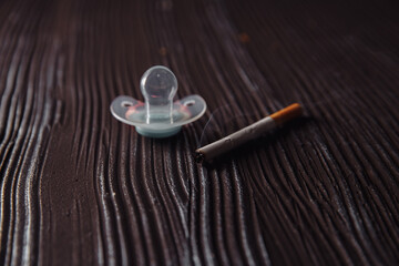 Stop smoking concept. Cigarette and baby pacifier on a dark wooden table.