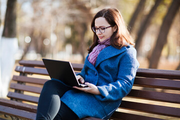 Happy  young woman working on laptop  in autumn at city park. 
