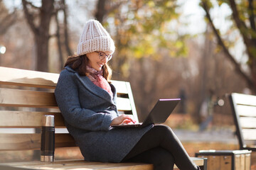 Happy  young woman working on laptop  in autumn at city park. 
