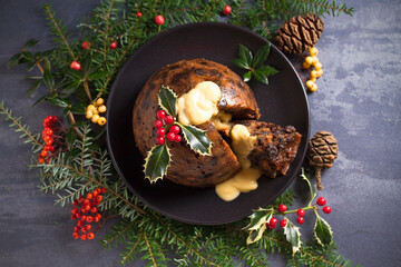 Richly spiced Christmas pudding cake with custard and Christmas decorations. Overhead, flat lay photo
