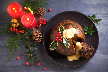 Richly spiced Christmas pudding cake with custard and Christmas decorations. Overhead, flat lay photo