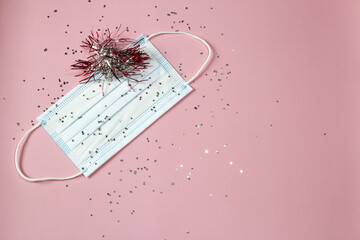 Hygienic face mask with confetti on a pink background. Christmas and New Year 2021 decor with space for text. Holidays self-isolation and coronavirus pandemic concept