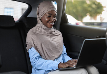 Business On The Go. Black Muslim Businesswoman Working On Laptop In Car