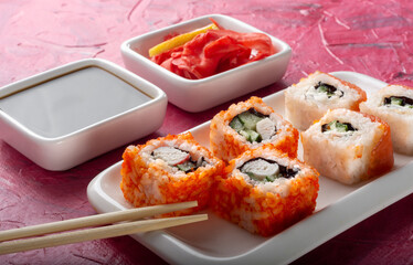 California and Philadelphia rolls on a white plate with ginger and soy sauce.