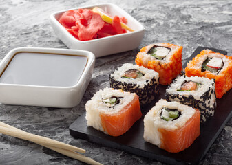 Different rolls on a black Board with soy sauce. Salmon rolls on a dark background.