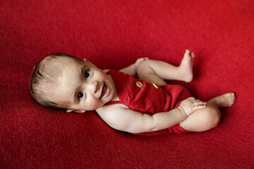 Cute newborn baby. Happy baby on a red background. Closeup portrait of newborn baby. Baby goods...