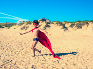 Little 9 year old child superhero with red cloak and glasses. Boy superhero on beach in summer vacation.