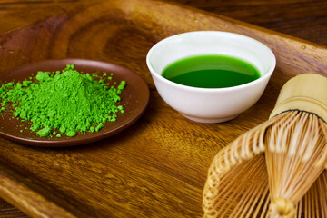 Green matcha tea in a cup with powdered matcha tea in a plate and bamboo matcha tea whisk also know as chasen on a wooden background. 