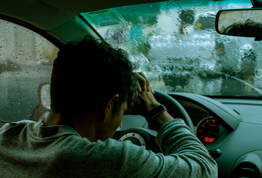 The Young Man Napping To Steering Wheel Of His Car With Depression Moodiness During Traffic Jam On Rainy Day.