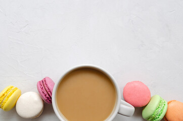 A cup of coffee with milk and multi-colored macarons on a light background with a place for text. Flat lay.