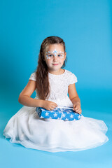 a girl in a white dress and with Christmas makeup on her face holding a blue gift isolated on an...