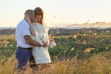 Happy pregnant couple in countryside on sunset - 389734572
