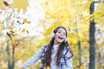 perfect autumn day of cheerful kid listen audio book or music wearing earphones in fall season park play with yellow fallen maple leaves, having fun
