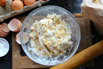 Hands kneading dough. Ball of dough on a rustic wooden background with dusting of flour. Dough with flour near broken egg with yolk in bowl and other utensil, ingredients lies on dark concrete table. 