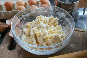 Hands kneading dough. Ball of dough on a rustic wooden background with dusting of flour. Dough with flour near broken egg with yolk in bowl and other utensil, ingredients lies on dark concrete table. 