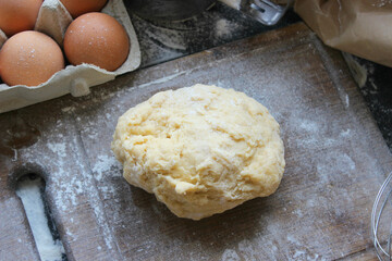 Hands kneading dough. Ball of dough on a rustic wooden background with dusting of flour. Dough with flour near broken egg with yolk in bowl and other utensil, ingredients lies on dark concrete table. 