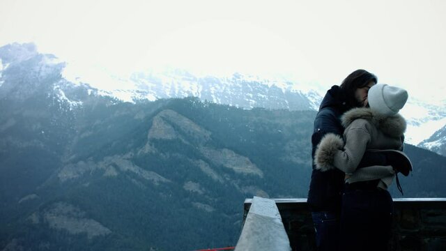 Couple kiss and look at the mountains in background. Romantic and beautiful scene in the winter season 4K