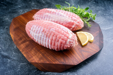 Modern Style traditioneller roher Rollbraten vom Kalb mit Kräutern und Zitronenscheiben  angeboten als close-up auf einem Design Holz Brett