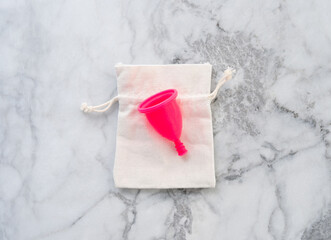 Pink menstrual cup on its storage cotton bag on marble table. Zero waste concept for female hygiene products.