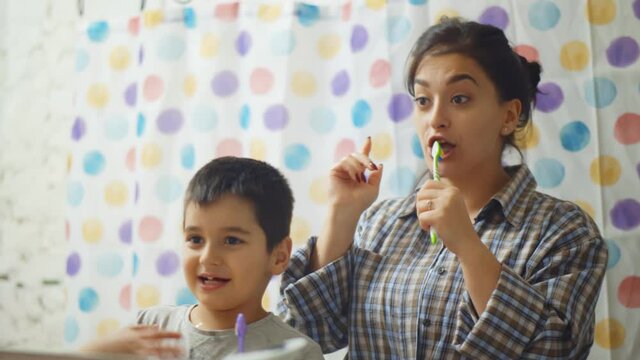 Portrait of happy young mother and son having fun and singing in toothbrush in bathroom