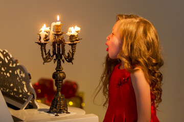 Charming long-haired girl sits at the piano and blows out the candle.