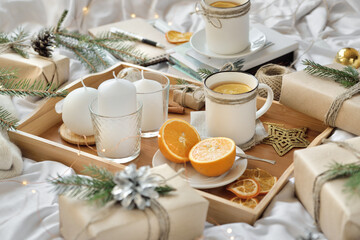 Cosy home flat lay composition with present boxes, blank copybook, a pen, tea and cones on a bed. Holiday shopping list, wish list or New Year Goals concept, presents checklist. Selective focus