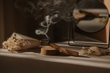  palo santo with jet of smoke, mirror and dried flowers on a neutral background. Abstract trendy picture. Minimalistic wabi sabi style.