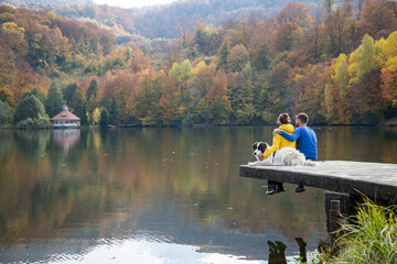 couple and dog sitting by beautiful autumn lake