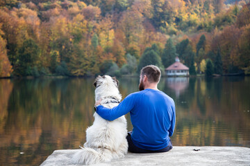 man and dog sitting by autumn lake social distancing