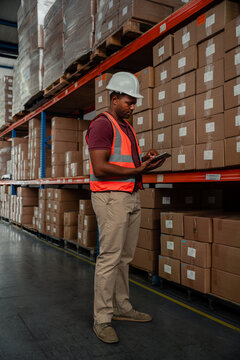 Ethnic Factory Worker Typing On Digital Ipad Researching Location Of Parcels Standing In Warehouse.