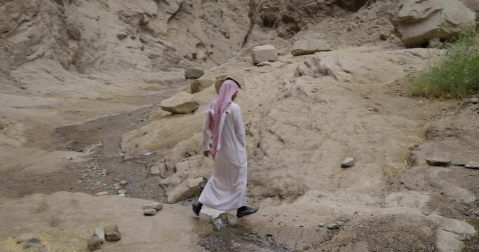Man in traditional Saudi Arabia clothing walks through river canyon, tracking shot
