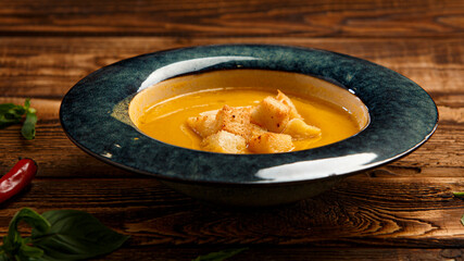Pumpkin cream soup with croutons on wooden background