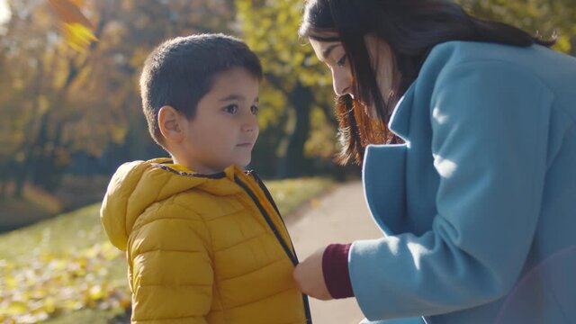 Side view of loving mother zipping jacket for little son outdoors