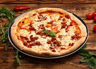 Pizza with meat and basil on a thin crust on a wooden background
