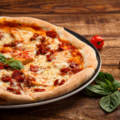 Pizza with meat and basil on a thin crust on a wooden background