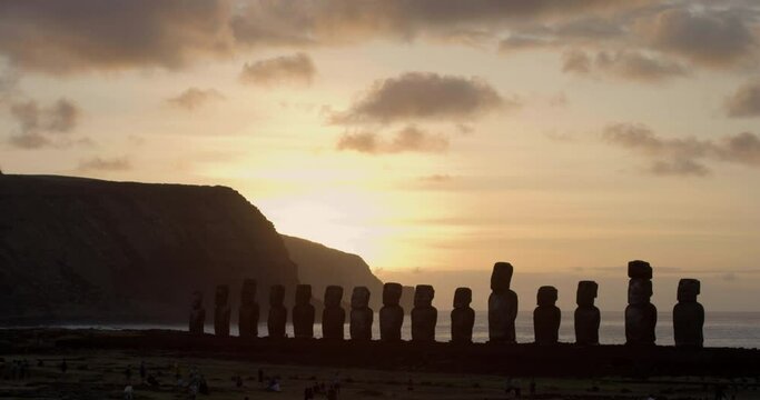 People admire Easter Island heads at sunset, wide