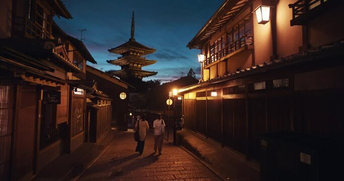 Kyoto, Japan with Kiyomizudera Temple in background, wide. People walk down dark alleyway