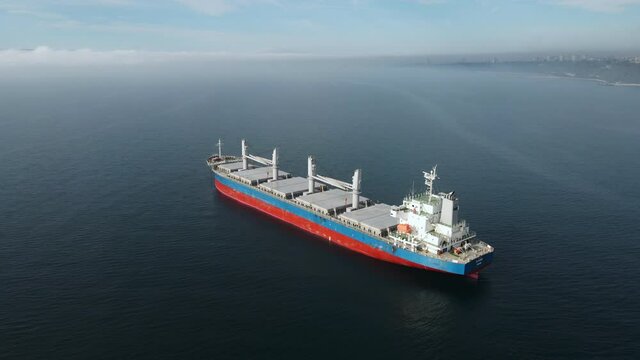 Aerial view bulk carrier docked of cargo ship, transports containers with goods, by sea sunset summer. Arrival of merchant ship in city seaport with crane