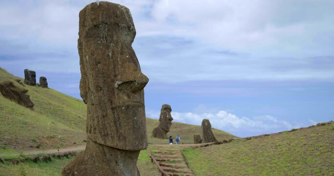 Tilt up, people walk past Easter Island head
