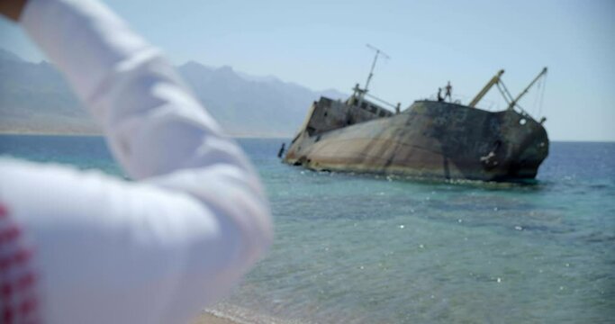 Close up, man wearing keffiyeh looks at shipwreck in Saudi Arabia