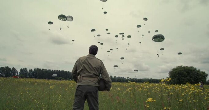 Tracking shot, WW2 soldier watches parachutes fall in Normandy field