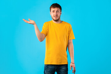 Confused puzzled young man shrugging at studio