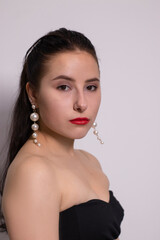 emotional portrait of attractive brunette in black top with white pearl earrings on white background.