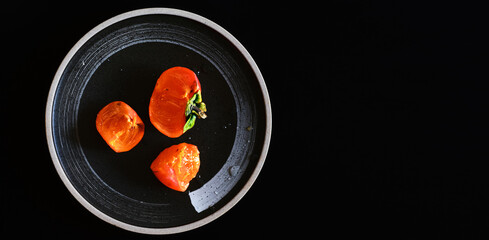 Persimmon and persimmon slices on a black plate, flat lay dark background. View from above. Place for text, autumn fruits, harvest. Copy space.