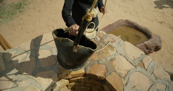 Tilt up, man picks up bucket from well in Saudi Arabia