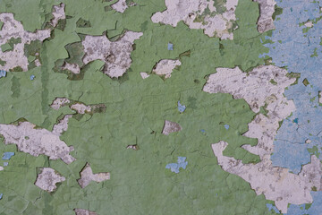 Green peeling paint on the wall. Old concrete wall with cracked flaking paint. Weathered rough painted surface with patterns of cracks and peeling. High resolution texture for background and design.