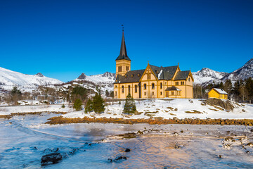 The wooden yellow Vågan Church on the beach on the Lofoten islands in Norway in winter with frozen...