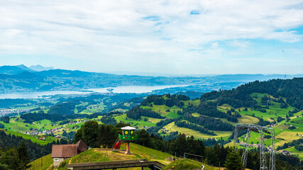 Paysage de montagne avec une vallée verdoyante,  des jeux, des arbres et de la forêt et des montagnes avec des cimes enneigées à l'arrière plan dans un ciel nuageux.