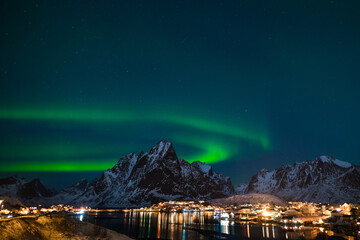 Dancing green polar lights over the village Reine on the Lofoten islands in Norway at night in winter with snow capped mountains